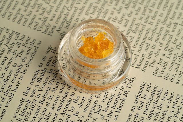 Yellow cannabis wax in a glass container on top of a piece of paper